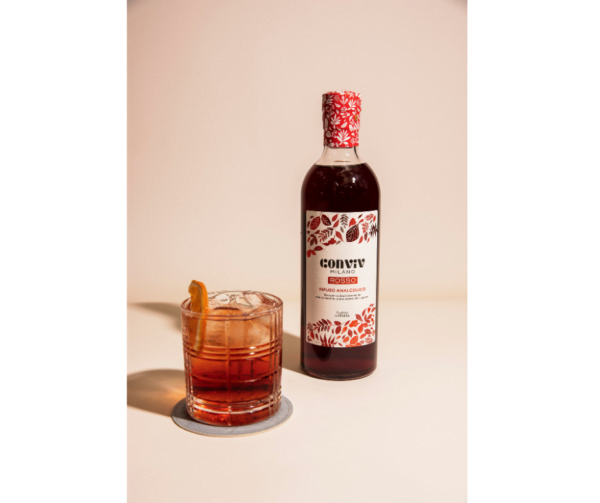 Een fles Conviv Rosso met een tumblerglas gevuld met een conviv cocktail gegarneerd met een schijfje sinaasappel.