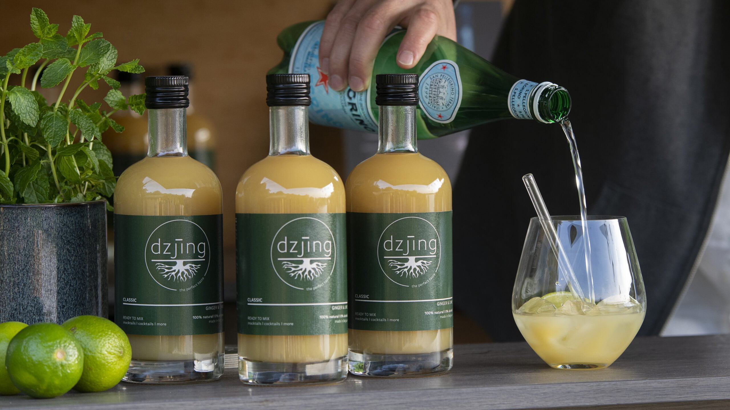 Drie flessen Dzjing op een rij met iemand die een lekkere alcoholvrije cocktail maakt met Dzjing.