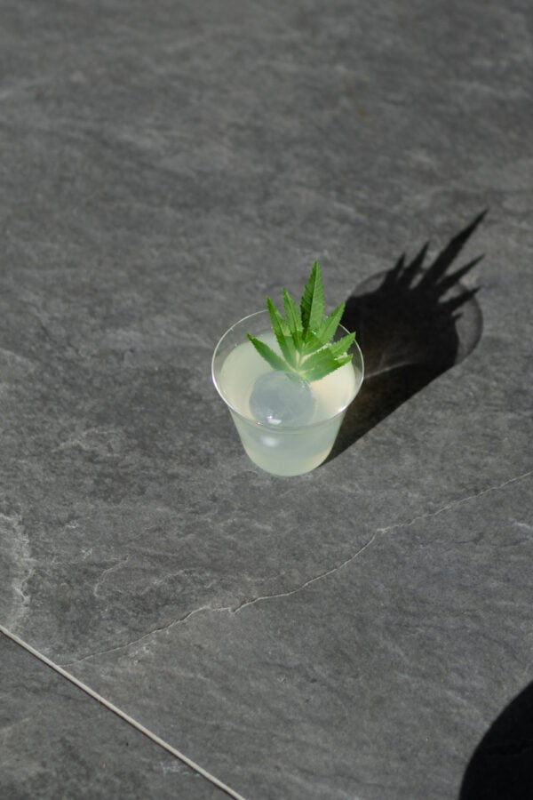 Een glas Wakataya alcoholvrije cocktail gepresenteerd op een marmeren ondergrond. In het glas een hazy witte drank met een groot ijsblokje en een blaadje huacatay.